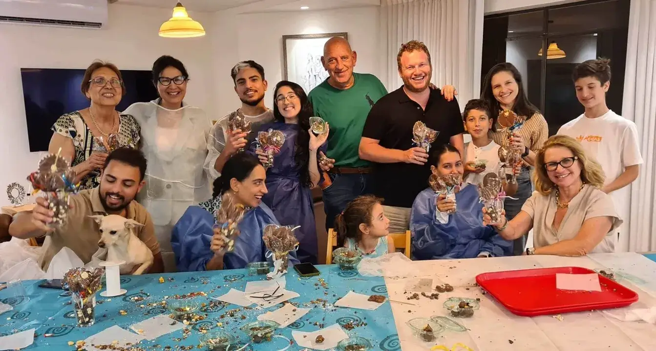 ילדים והורים משתתפים יחד בפעילות מהנה סביב שולחן השוקולד.