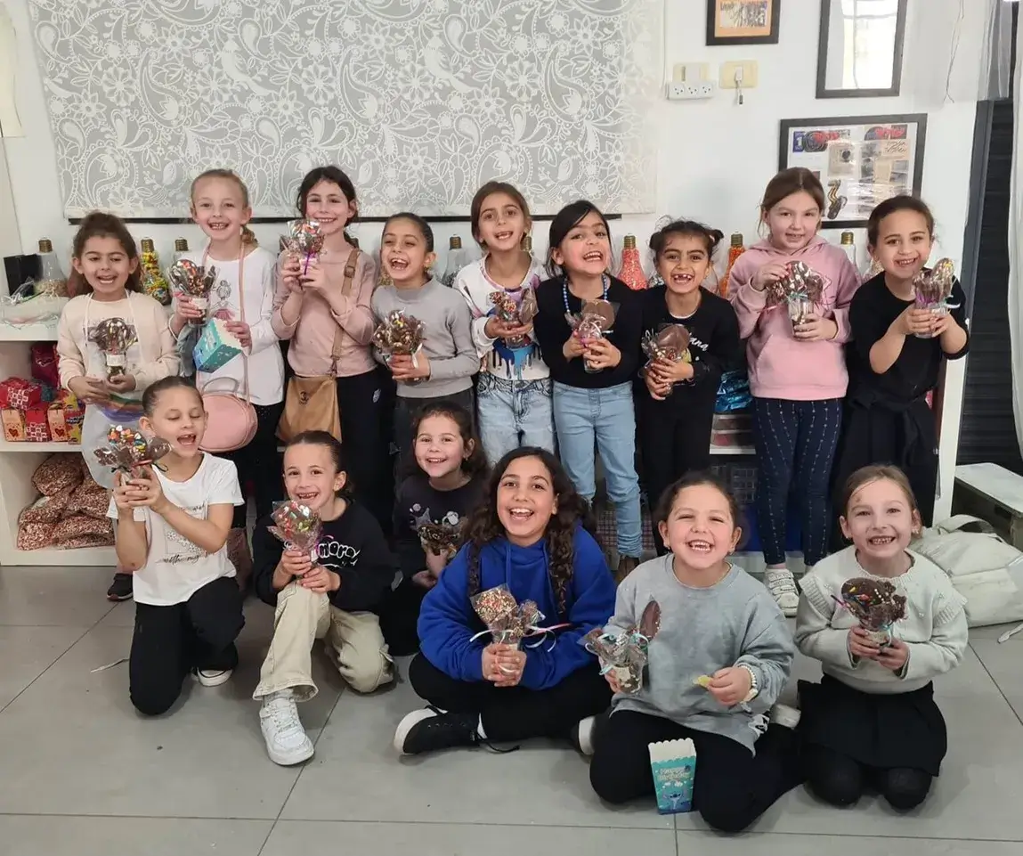 ילדים מכינים שוקולדים צבעוניים בסדנת שוקולד.
