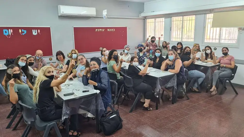 סדנת שוקולד בעינביז שוקולד - עובדים יושבים סביב שולחן ומכינים שוקולדים ביום גיבוש.
