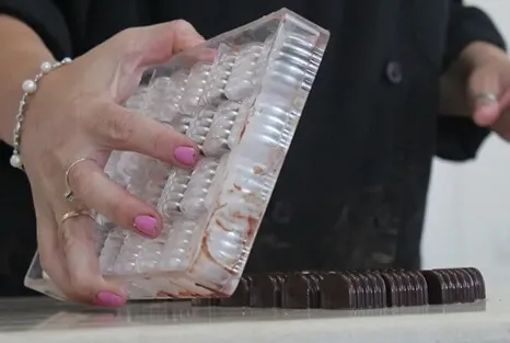 שוקולטיירית (רוני כהנא) מוציאה פרלינים מבריקים מתבנית מקצועית בסדנת שוקולד של עינביז